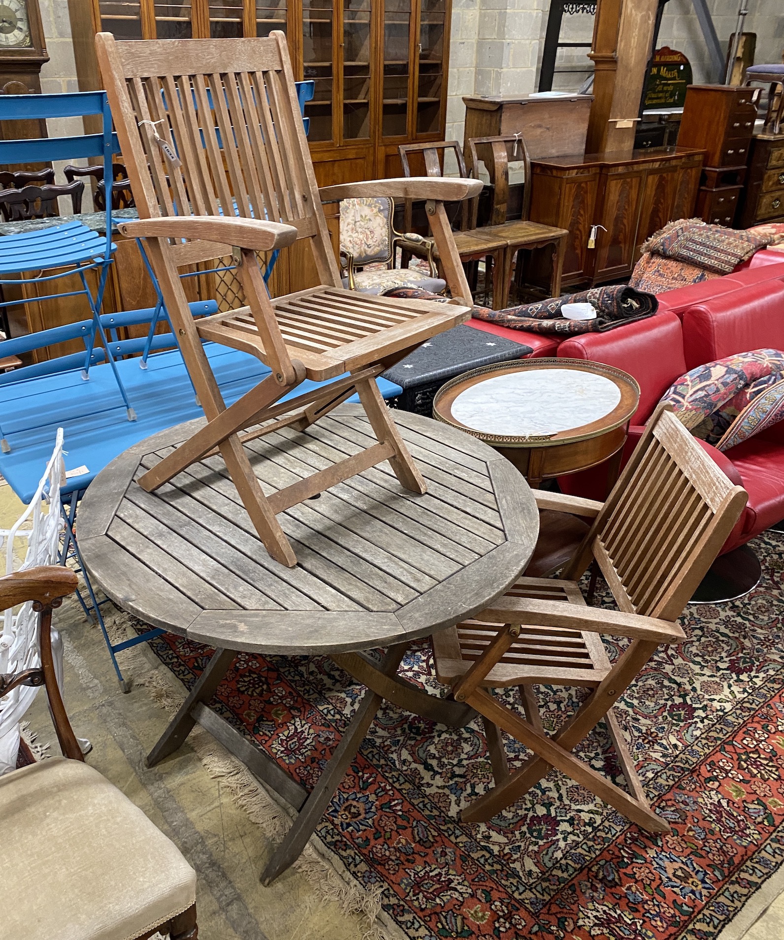 A circular weathered teak folding garden table, diameter 100cm, height 73cm and two elbow chairs